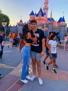 a man and woman standing in front of a castle at disney world kissing each other