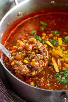 a ladle full of chili and meat stew with corn on the side, ready to be eaten