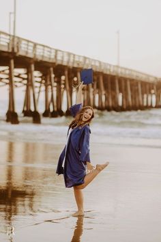 a woman is standing on the beach with her legs in the air and holding up a book