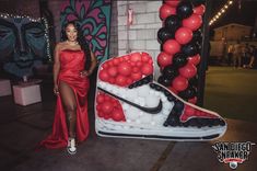 a woman in a red dress standing next to a giant nike shoe with balloons on it