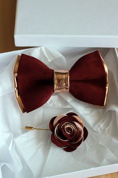 a red bow tie sitting on top of a white box next to a brown rose