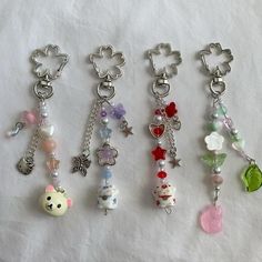 four key chains with charms attached to them on a white cloth covered tablecloth in various shapes and sizes