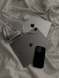 an apple laptop, headphones and iphone on a white bed sheet with the covers pulled down