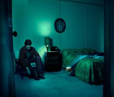 a woman sitting on a chair in a dark room next to a bed and lamp