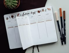 an open planner with pens and markers on it next to a potted cacti