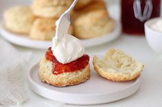 a plate topped with scones covered in cream and strawberry jam next to other pastries