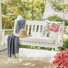 a white porch swing with a hat and throw pillow on it next to pink flowers