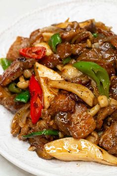 a white plate topped with meat and veggies on top of pasta covered in sauce