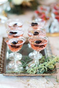 four glasses filled with different types of drinks on a tray next to flowers and herbs