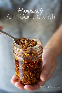 a person holding a jar filled with chili garlic crumbs and a spoon in it