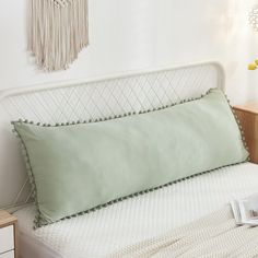 a white bed topped with green pillows next to a night stand