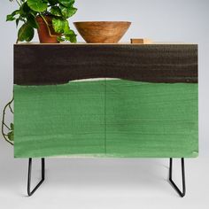 a green cabinet with a potted plant on top and a wooden bowl sitting on top