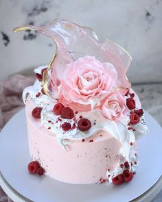 a pink cake with white frosting, raspberries and flowers on the top