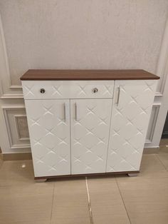 a white cabinet with wood top and diamond patterning on it's sides, in front of a wall