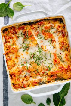 a casserole dish with spinach and cheese on top, surrounded by leaves