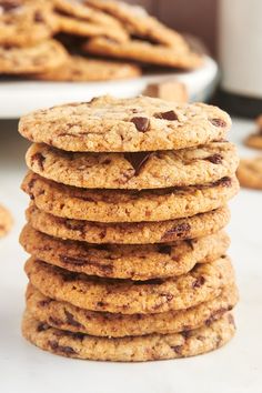 chocolate chip cookies stacked on top of each other in front of a plate of cookies