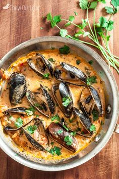 a pan filled with mussels and sauce on top of a wooden table next to parsley