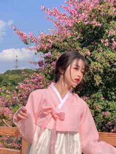 a woman in a pink and white kimono standing on a wooden bench next to flowers