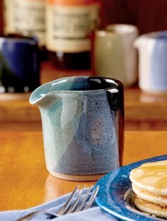 a blue and white pitcher sitting on top of a wooden table next to some pancakes