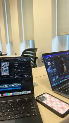 two open laptops sitting on top of a table next to an iphone and cell phone