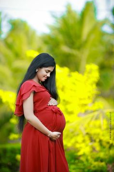 a pregnant woman in a red dress poses for the camera with her hands on her belly