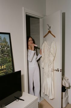 a woman standing next to a white dress on a hanger in front of a tv