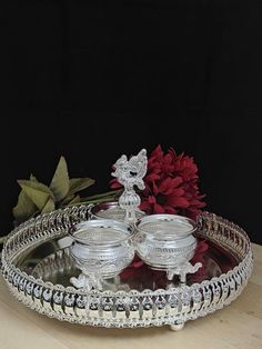 two silver dishes on a tray with flowers in the background