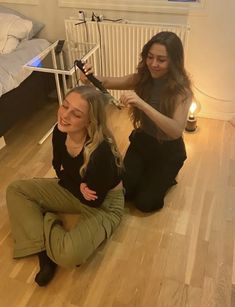 two women are sitting on the floor and one is blow drying her hair