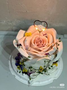 a white cake with a pink rose on top and some yellow flowers around the base