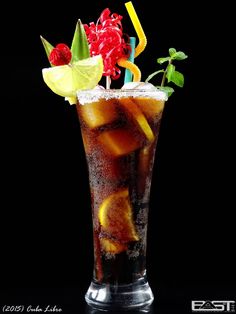 a tall glass filled with ice and fruit on top of a black table next to two colorful straws