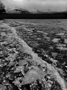 an ice covered river with mountains in the backgroung and clouds in the sky