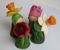 three little felt dolls with flowers on them sitting next to each other in front of a white background