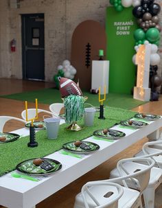 a table set up for a football party with plates, cups and balloons in the background