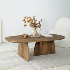 a vase with dried flowers sitting on top of a wooden table next to a white chair