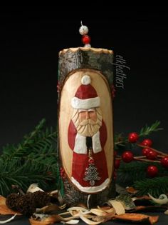 a wooden christmas ornament with a santa clause on it's face, surrounded by pine needles and red berries