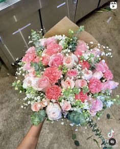 a bouquet of pink and white flowers is held by someone's hand in front of an oven