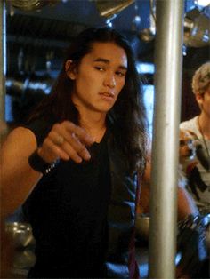 two young men standing next to each other in front of a metal rack filled with pots and pans