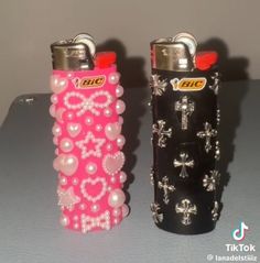 two lighters are decorated with pearls and cross designs on them, one is pink and the other is black