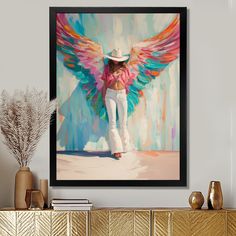 a painting of a woman in white jeans and a cowboy hat with colorful wings on the wall