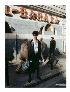 a man standing on the sidewalk in front of a building with people walking past him