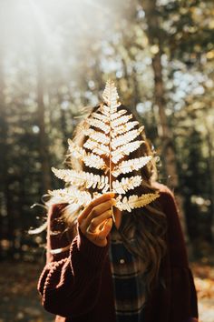 a woman holding a leaf in front of her face with the sun shining behind her