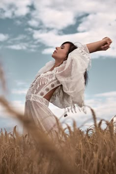 a woman standing in a field with her arms spread out and looking up into the sky