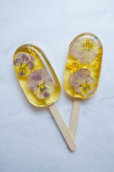 two lollipops with yellow and purple flowers on them sitting on a white surface