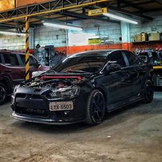 two cars parked in a garage with their hoods open