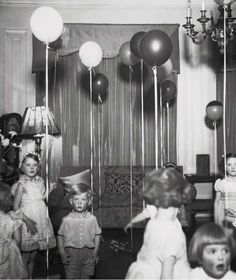 an old black and white photo of children at a party with balloons in the air