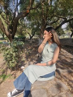 a woman sitting on top of a rock talking on a cell phone while holding her hand up to her ear