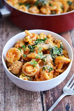 two bowls filled with pasta and spinach on top of a wooden table next to silverware