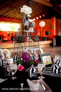 a birdcage filled with flowers sitting on top of a table next to wine glasses