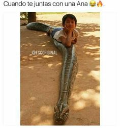 a boy laying on top of a large snake in the dirt with his arm around him