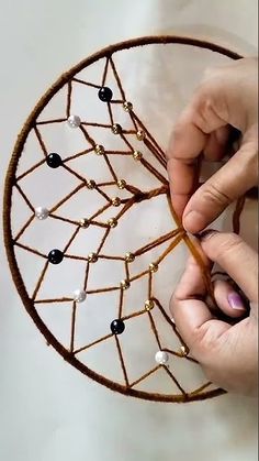 two hands are working on a piece of art with beads and wire in the shape of a leaf